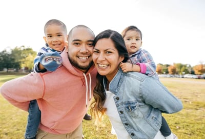 Familia sonriente disfrutando al aire libre con niños sobre los hombros de sus padres