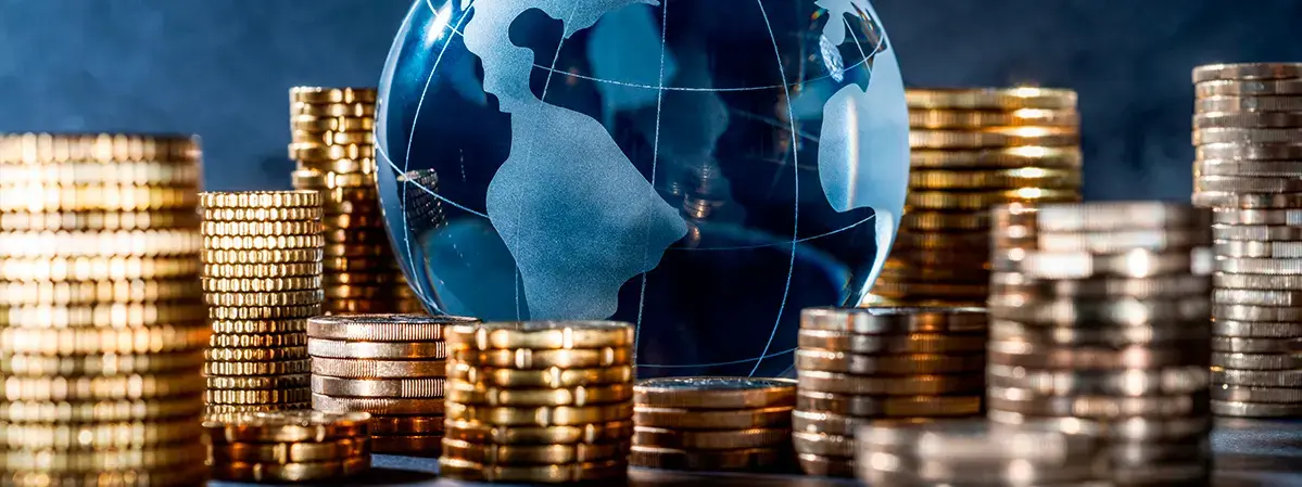 Globo terráqueo de cristal rodeado por pilas de monedas doradas, representando finanzas internacionales y crecimiento económico.