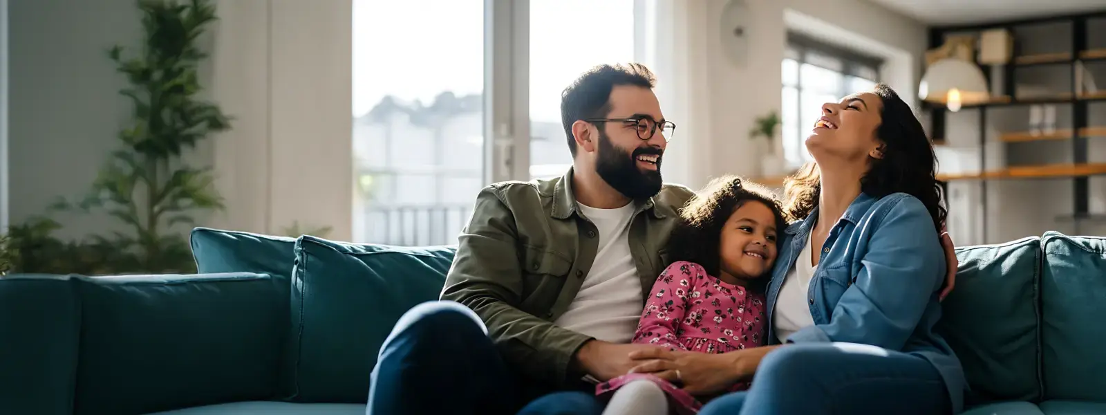 Foto de familia (madre, padre e hija) sonriendo y abrazándose felizmente en el sofá de su hogar, representando la tranquilidad y protección que ofrece BN Seguros en su aniversario.