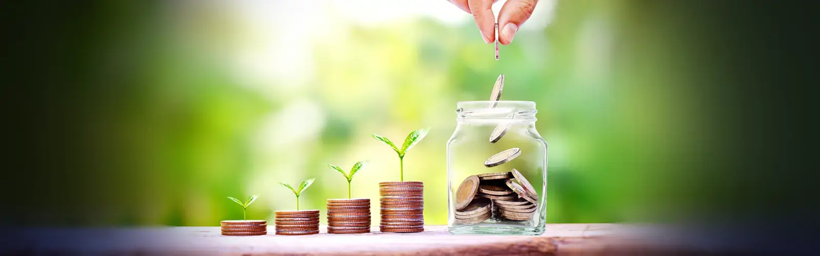 Mano colocando una moneda en un frasco lleno de monedas junto a pilas de monedas con pequeñas plantas creciendo sobre ellas.