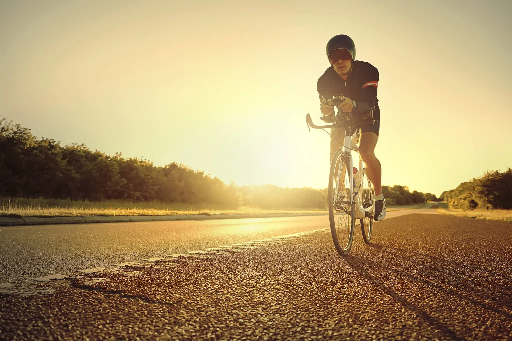 Ciclista con casco y gafas de sol pedaleando en carretera al amanecer.