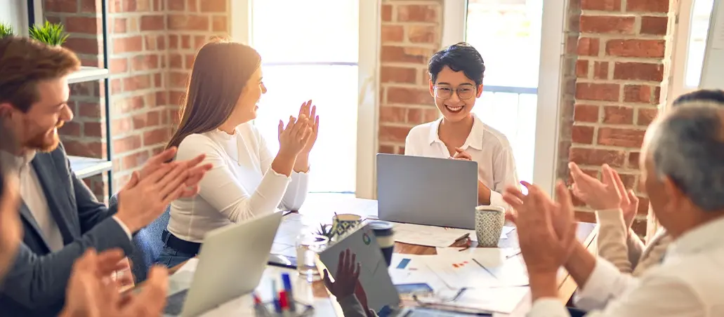Equipo de trabajo aplaudiendo a una mujer frente a su laptop en una reunión
